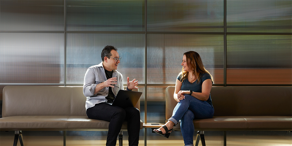 Two colleagues in conversation, sitting on benches in a common area.