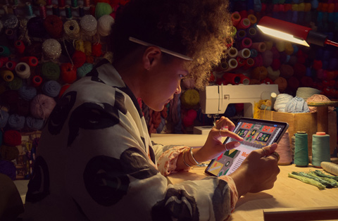 Osoba sedící u stolu si pomocí dvou prstů přibližuje obrázek na iPadu.