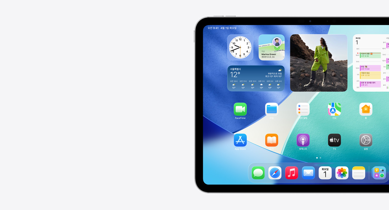 가로 방향으로 놓인 iPad. 왼쪽 화면에는 Liquid Glass 효과가 적용된 반투명 시계, 나의 찾기 앱, 날씨 위젯, 두 줄로 정렬된 작은 앱 아이콘, Dock이 표시된 홈 화면