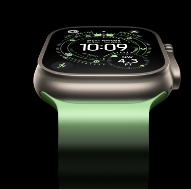 A close-up of a Natural Titanium Apple Watch Ultra 3 on a black background. The display shows the time and other dynamic info.