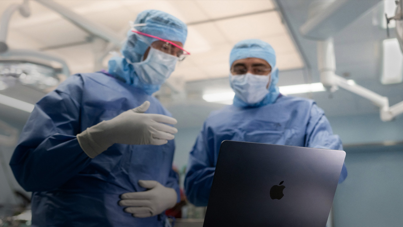 Two surgeons discussing something on the screen of a MacBook Pro in the operating room.