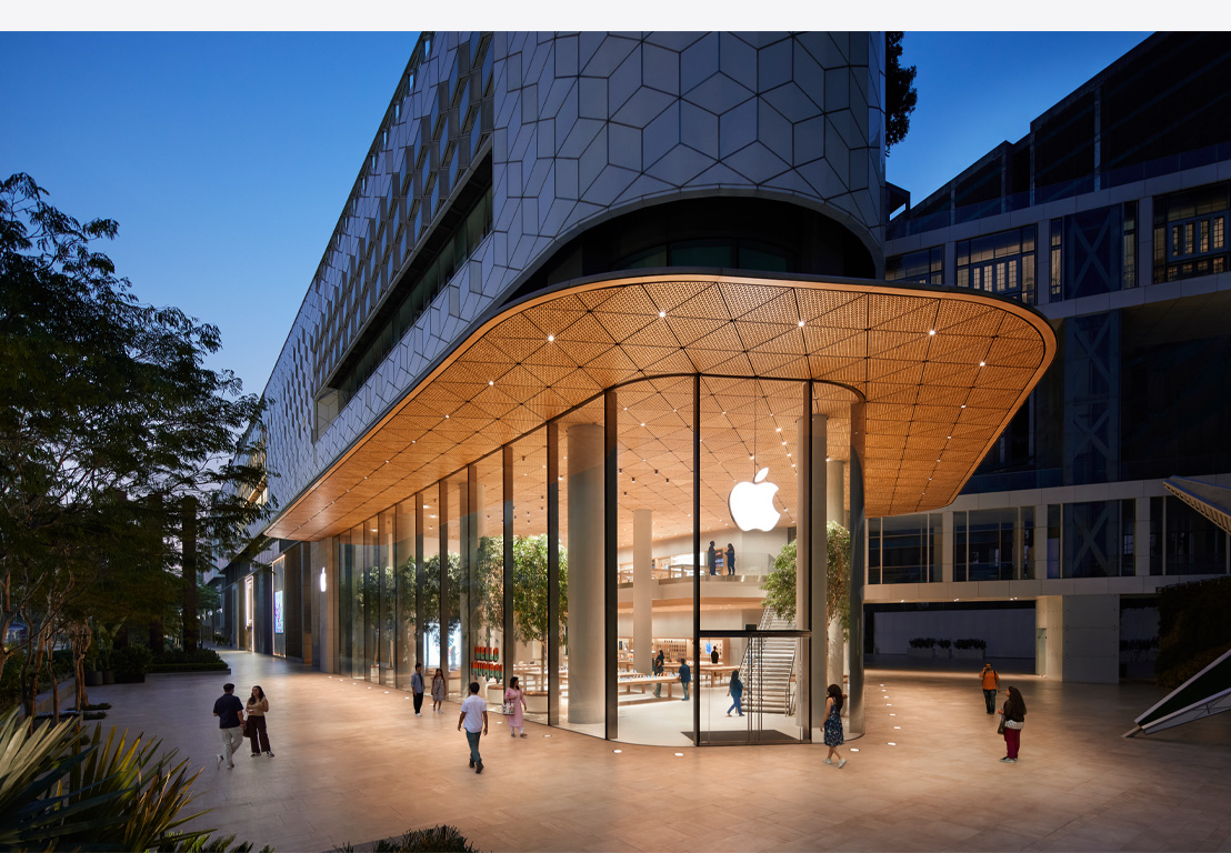 Apple Store τη νύχτα, γυάλινα παράθυρα, φωτισμένο εσωτερικό, λογότυπο Apple στο κέντρο της μπροστινής πόρτας.