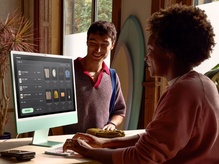 Dua orang di ruangan yang terang, satu di antaranya memeriksa pesanan di iMac M4 berwarna hijau.
