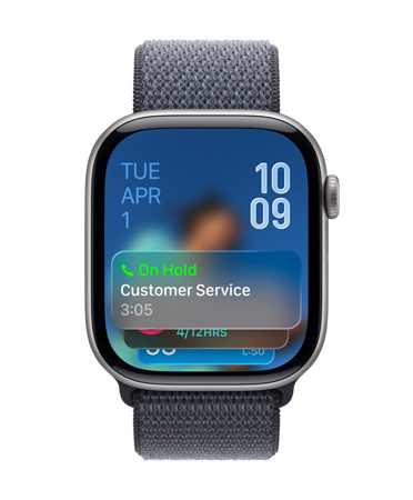 Apple Watch w kolorze onyksu z paskiem w kolorze szałwii. Na dole ekranu widać powiadomienie Asystenta oczekiwania. W lewym górnym rogu widać datę, a w prawym górnym rogu godzinę w orientacji pionowej.